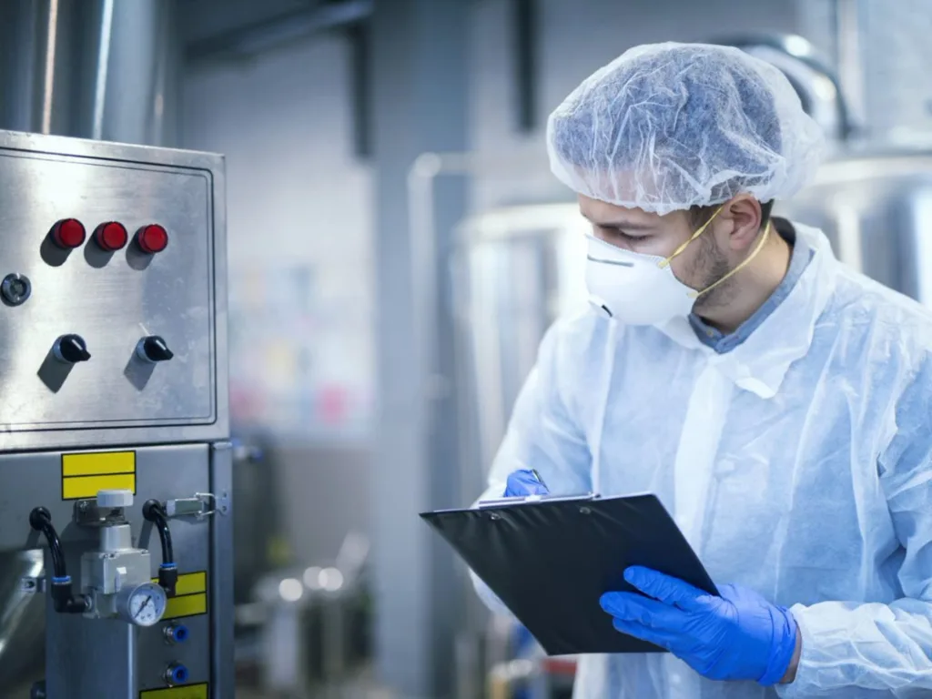 Scientist wearing gloves, mask and a lab coat checking the temperature on a machine in a laboratory